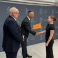 Na fotografii wójt składa gratulacje absolwentce technikum. Na zdjęciu także dyrektor szkoły z Przemętu. W tle ścianka gminy.
