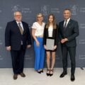 Na zdjęciu wójt, absolwentka szkoły podstawowej, która pozuje z listem gratulacyjnym oraz dyrektor szkoły z Przemętu. W tle ścianka gminy.
