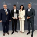 Na zdjęciu wójt, absolwent szkoły podstawowej, który pozuje z listem gratulacyjnym oraz dyrektor szkoły z Przemętu. W tle ścianka gminy.