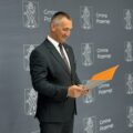Na fotografii uśmiechnięty wójt, który spogląda na list, który wręczy jednemu z uczniów. w tle ścianka gminy.