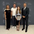 Na zdjęciu wójt, absolwentka szkoły podstawowej, która pozuje z listem gratulacyjnym oraz dyrektorka szkoły z Kaszczoru. W tle ścianka gminy.