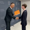 Na fotografii wójt składa gratulacje absolwentowi szkoły podstawowej. W tle ścianka gminy.