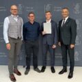 Na zdjęciu wójt, absolwent szkoły podstawowej, który pozuje z listem gratulacyjnym oraz dyrektor szkoły z Bucza. W tle ścianka gminy.