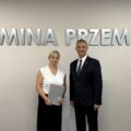 Wójt pozuje do zdjęcia z jedną z mianowanych nauczycielek. Kobieta trzyma akt mianowania w ręce. w tle srebrny napis "Gmina Przemęt" oraz flaga z herbem gminy.