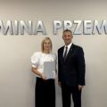 Wójt pozuje do zdjęcia z jedną z mianowanych nauczycielek. Kobieta trzyma akt mianowania w ręce. w tle srebrny napis "Gmina Przemęt" oraz flaga z herbem gminy.