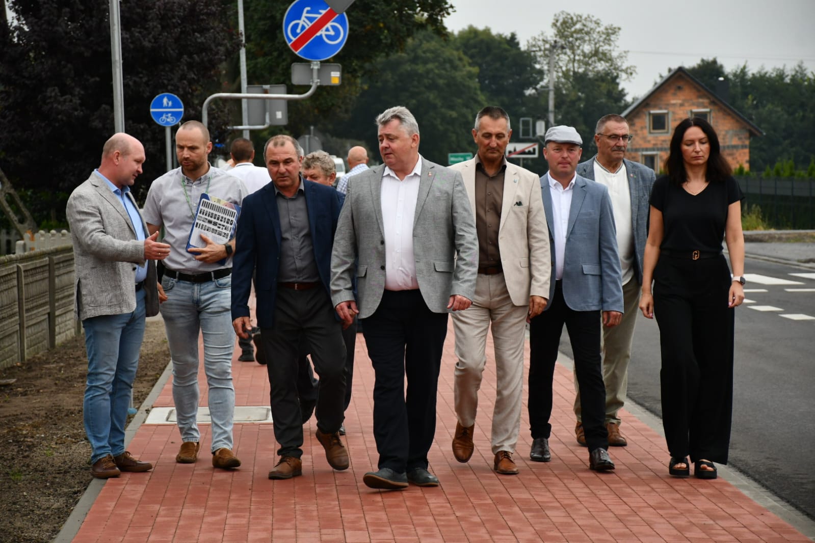 Na fotografii osoby uczestniczące w oficjalnym otwarciu drogi i ścieżki rowerowej. Na zdjęciu osoby te podążają wzdłuż ścieżki.