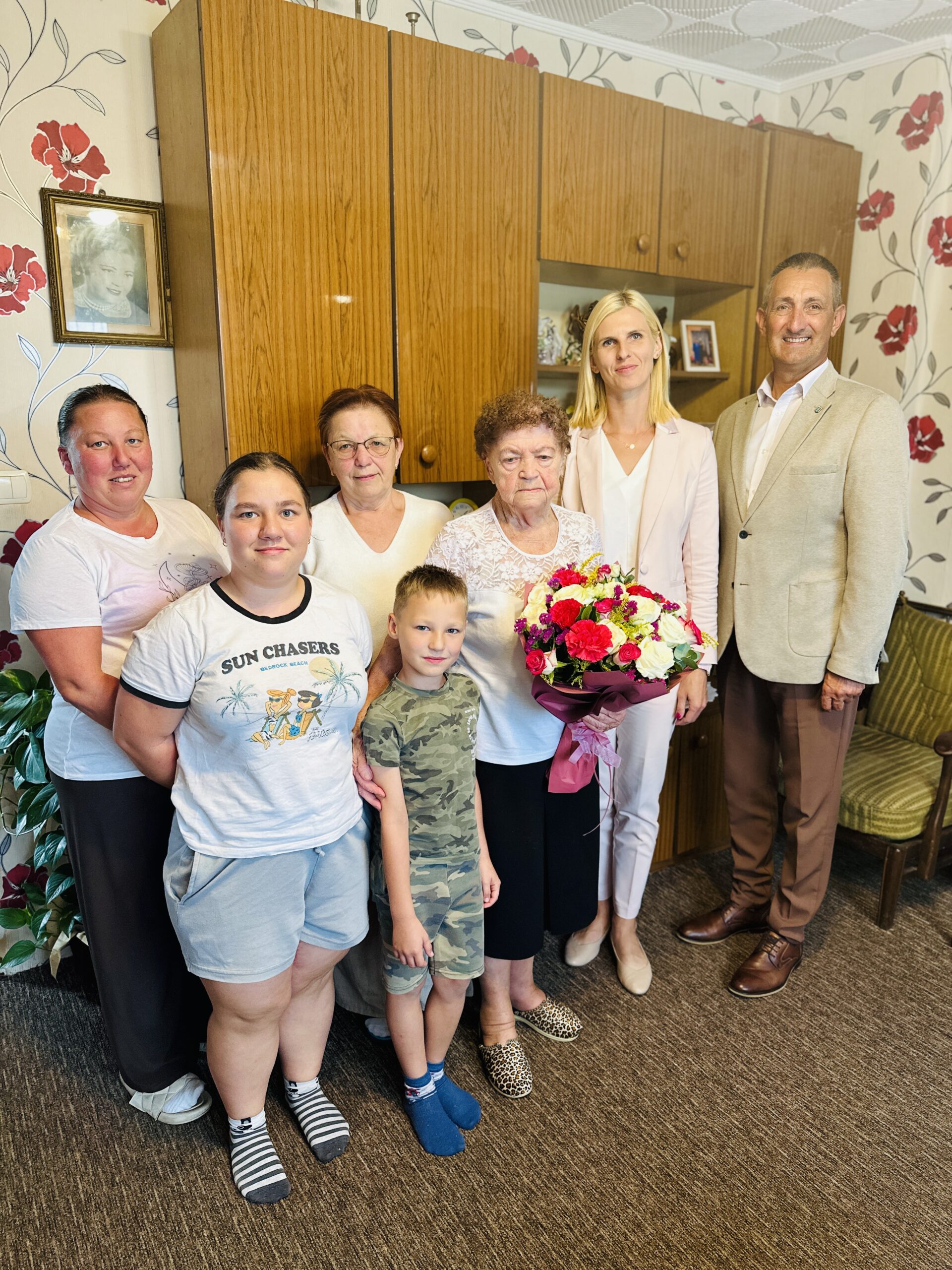 Wspólne zdjęcie, na którym znajduje się wójt, zastępca kierownika USC Irena Mikołajczak, jubilatka, która trzyma bukiet kwiatów oraz członkowie jej rodziny.
