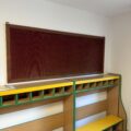 Zdjęcie przedstawia szatnię dla dzieci. Widoczny regał z kolorowymi szufladami i wieszakami, tuż nad nim wisi czerwona tablica korkowa.
