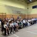 Na zdjęciu ukazani uczniowie wraz z rodzicami, którzy siedzą na krzesłach w sali gimnastycznej w Buczu podczas rozpoczęcia roku.