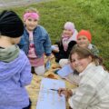 Grupa dziewczynek siedzi na kocu i rozwiązuje zagadkę.