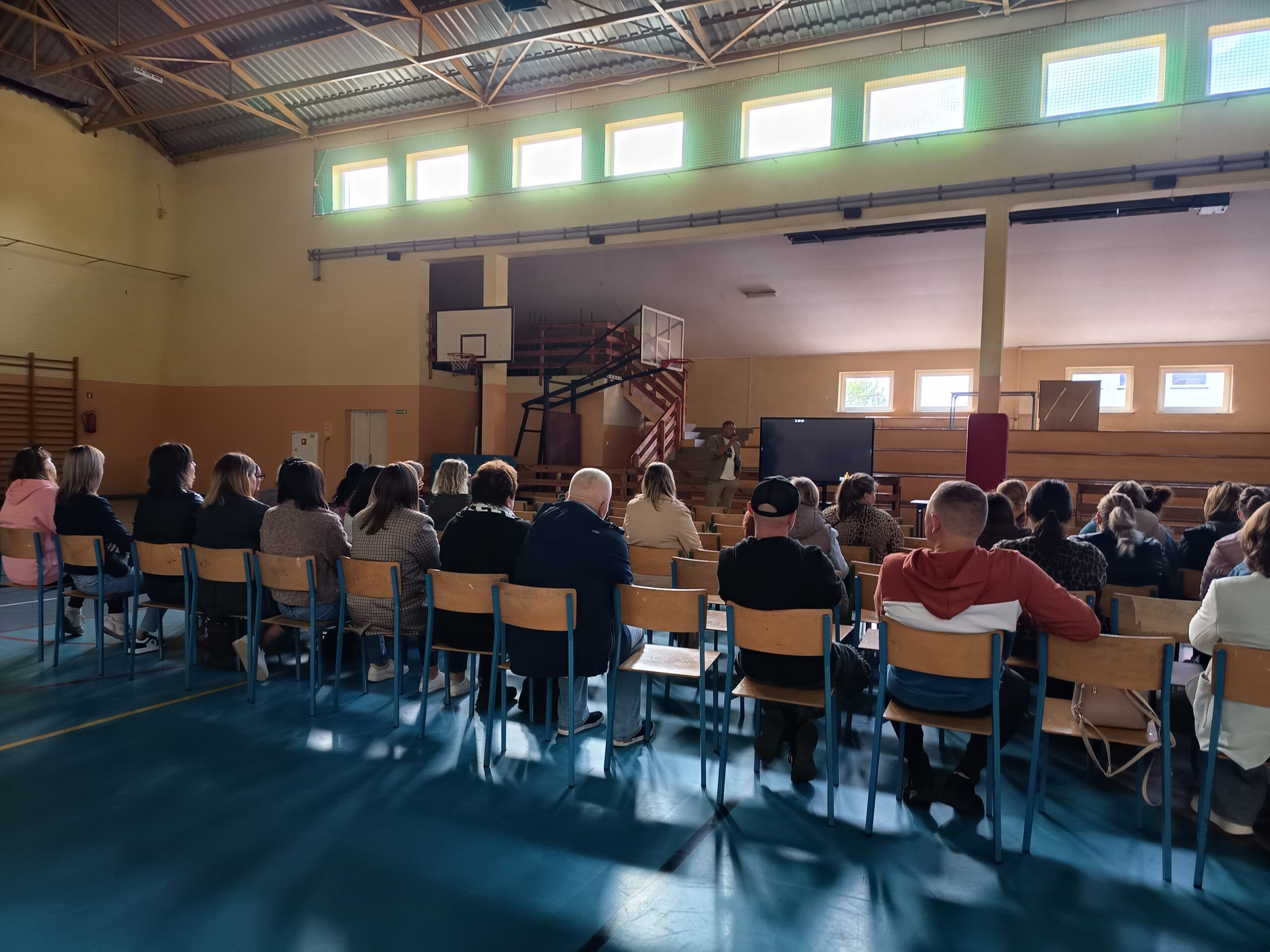 Na fotografii widoczne osoby siedzące na widowni i osoba prowadząca prelekcje.
