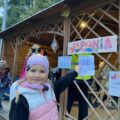 Dziewczynka patrzy w kierunku kamery i ręką wskazuję na napisy za nią.
