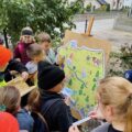Grupa dzieci stoi przy sztaludze, na której widnieje kreskówkowa mapa Polski