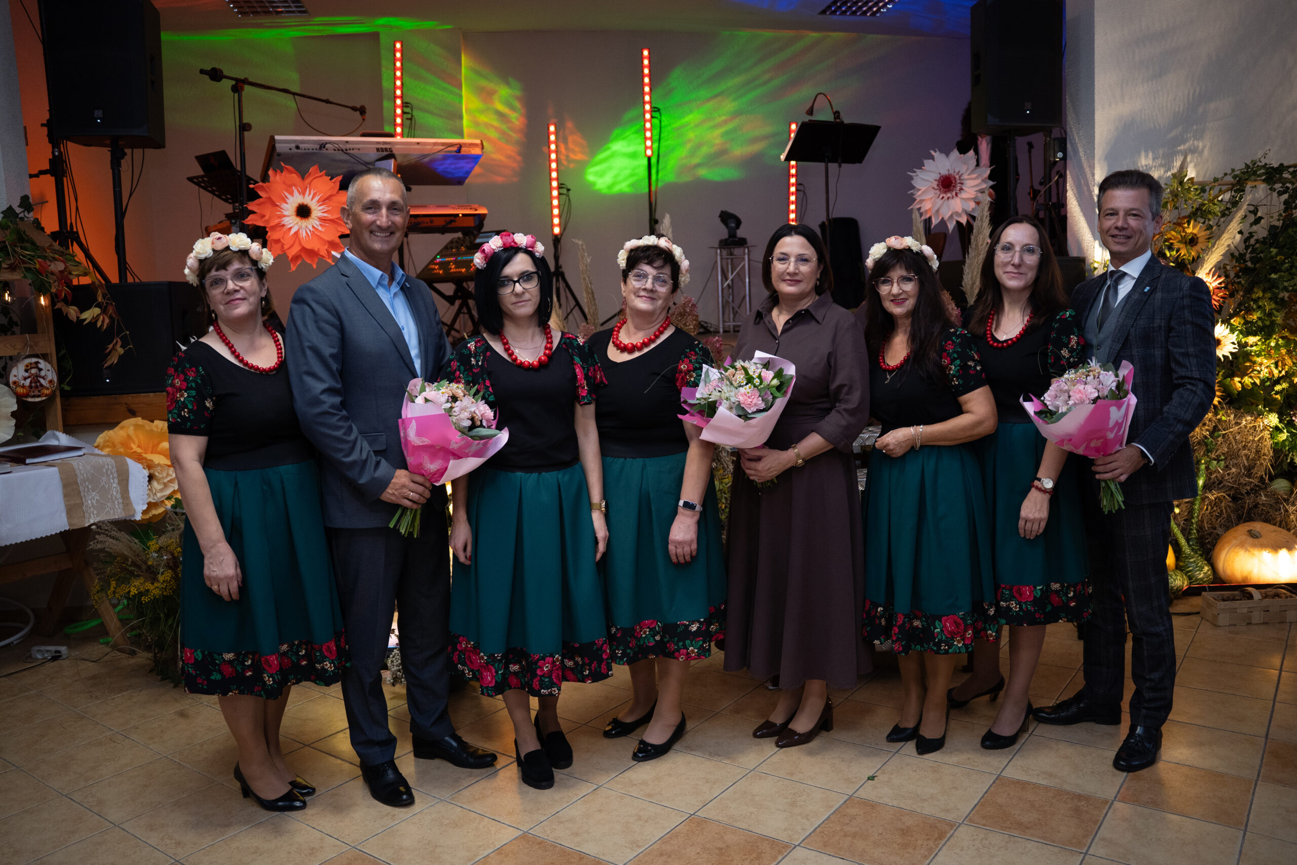 Na fotografii kobiety z KGW ubrane w ludowe stroje. Na zdjęciu także: wójt gminy, zastępca wójta oraz skarbnik gminy, którzy pozują z bukietami kwiatów.