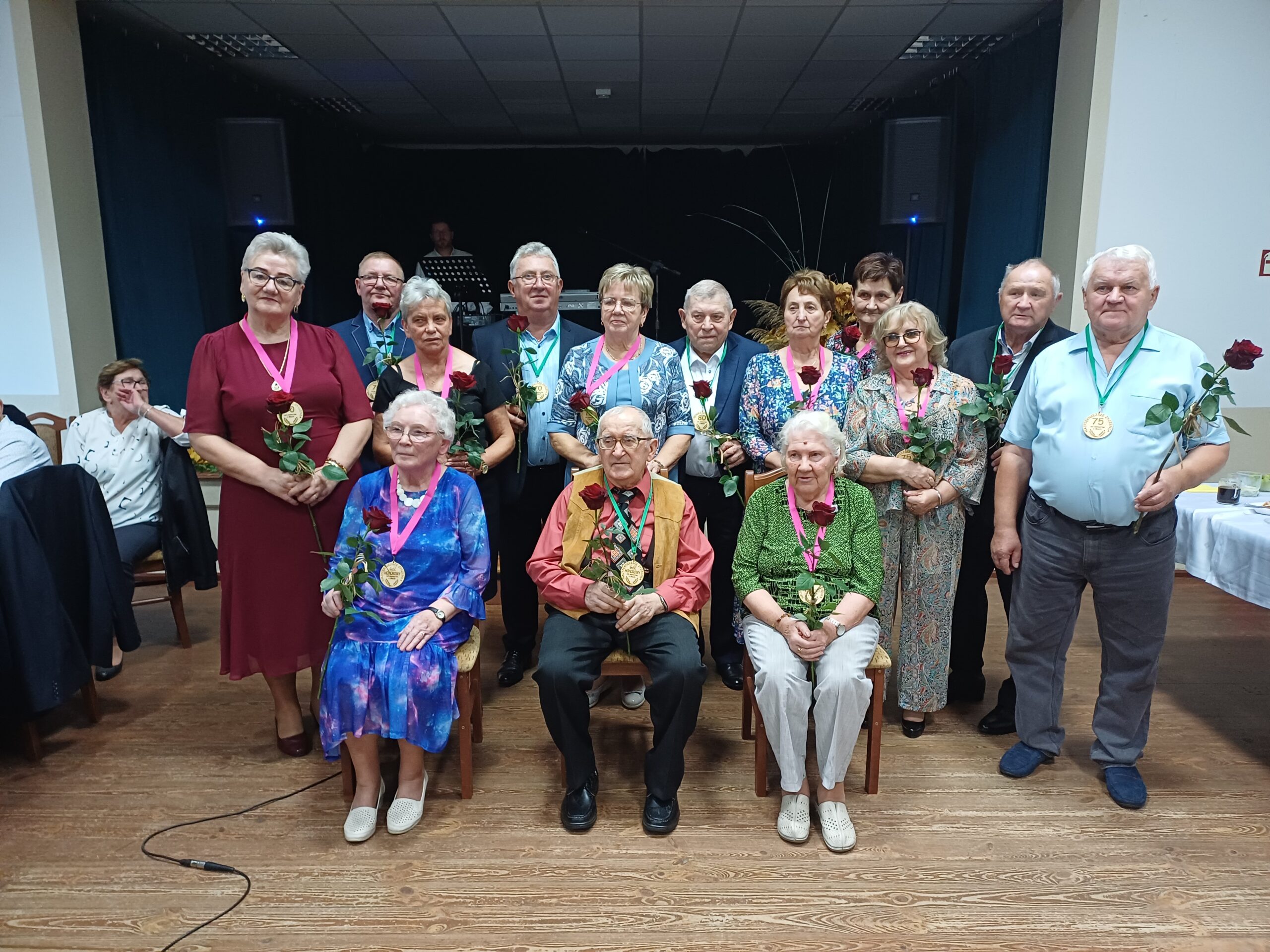 Na zdjęciu widoczni seniorzy, którzy pozują z różami i medalami.