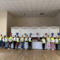Na fotografii uczniowie podczas występu artystycznego. Każdy z nich trzyma jedną literkę, która razem z pozostałymi tworzy zdanie „Odblaskowa szkoła”.