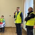 Na zdjęciu widoczni policjanci, jeden z nich przemawia podczas spotkania.