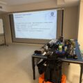 Na zdjęciu widoczny jest projektor, na którym wyświetlana jest prezentacja oraz widoczny jest stół, na którym poukładane są przedmioty potrzebne do szkolenia.