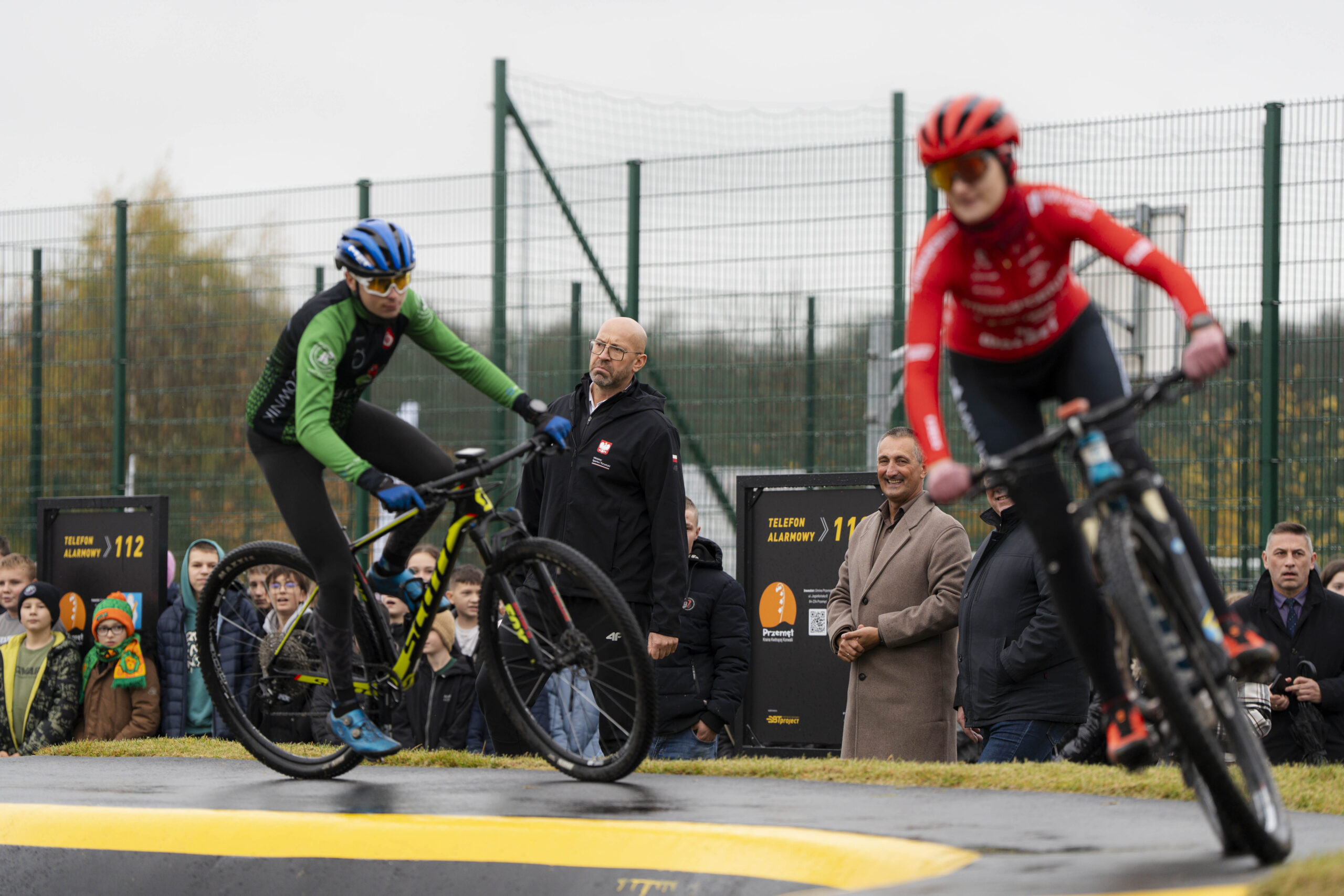 Na zdjęciu dwóch rowerzystów podczas pokazowego przejazdu na pumptracku. W tle osoby uczestniczące w otwarciu.