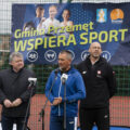 Zdjęcie przedstawia wójta Janusza Frąckowiaka podczas przemowy na konferencji prasowej na orliku. Obok wójta stoją minister sportu i turystyki oraz starosta powiatu wolsztyńskiego. W tle baner "Gmina Przemęt wspiera sport".