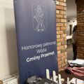 Na zdjęciu widoczne statuetki medale oraz upominki. Widoczny także roll-up informujący o honorowym patronacie.