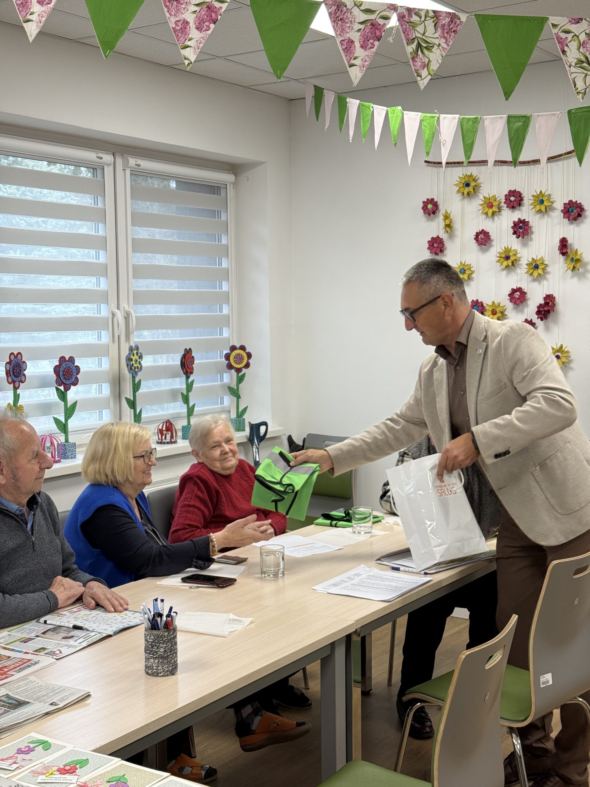 Na zdjęciu widoczny wójt, który rozdaje odblaskowe kamizelki seniorom.