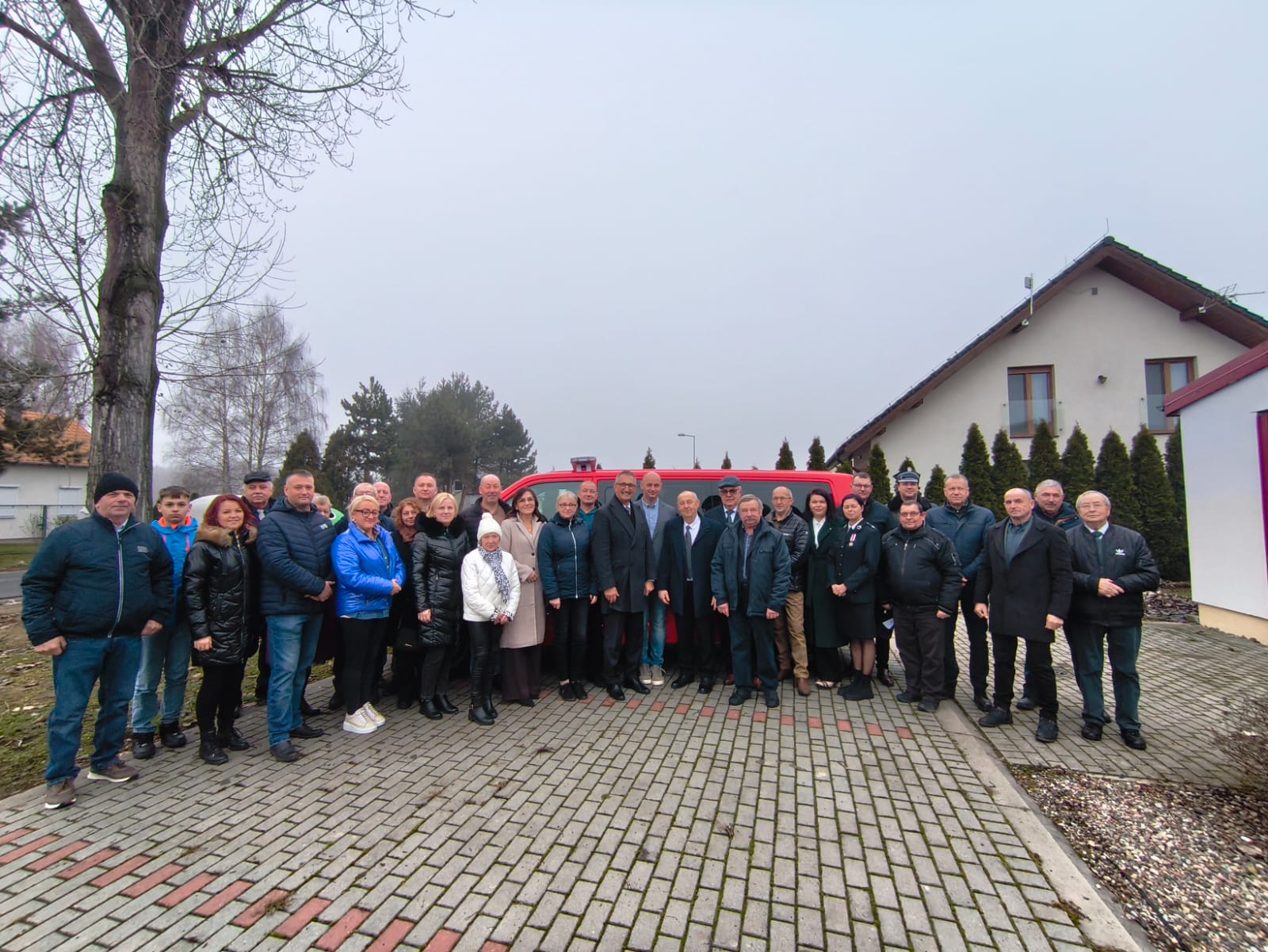Grupowe zdjęcie wszystkich osób przybyłych na uroczystość. W tle samochód strażacki.