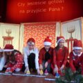 Zdjęcie przedstawia występ artystyczny uczniów z Kaszczoru na scenie, przebranych w świąteczne stroje.
