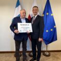 Na fotografii wójt wraz z sołtysem Olejnicy pozują z czekiem. W tle widoczne są flagi: Polski, Unii Europejskiej oraz z herbem gminy Przemęt.