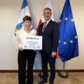 Na fotografii wójt wraz z sołtysem Osłonina pozują z czekiem. W tle widoczne są flagi: Polski, Unii Europejskiej oraz z herbem gminy Przemęt.
