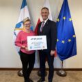 Na fotografii wójt wraz z sołtysem Perkowa pozują z czekiem. W tle widoczne są flagi: Polski, Unii Europejskiej oraz z herbem gminy Przemęt.