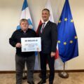 Na fotografii wójt wraz z sołtysem Popowa Starego pozują z czekiem. W tle widoczne są flagi: Polski, Unii Europejskiej oraz z herbem gminy Przemęt.