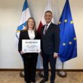 Na fotografii wójt wraz z sołtysem Przemętu pozują z czekiem. W tle widoczne są flagi: Polski, Unii Europejskiej oraz z herbem gminy Przemęt.