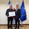 Na fotografii wójt wraz z sołtysem Radomierza pozują z czekiem. W tle widoczne są flagi: Polski, Unii Europejskiej oraz z herbem gminy Przemęt.