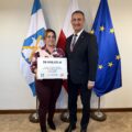 Na fotografii wójt wraz z sołtysem Sączkowa pozują z czekiem. W tle widoczne są flagi: Polski, Unii Europejskiej oraz z herbem gminy Przemęt.