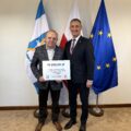 Na fotografii wójt wraz z sołtysem Sokołowic pozują z czekiem. W tle widoczne są flagi: Polski, Unii Europejskiej oraz z herbem gminy Przemęt.