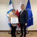 Na fotografii wójt wraz z sołtysem Solca Nowego pozują z czekiem. W tle widoczne są flagi: Polski, Unii Europejskiej oraz z herbem gminy Przemęt.