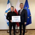 Na fotografii wójt wraz z sołtysem Starkowa pozują z czekiem. W tle widoczne są flagi: Polski, Unii Europejskiej oraz z herbem gminy Przemęt.
