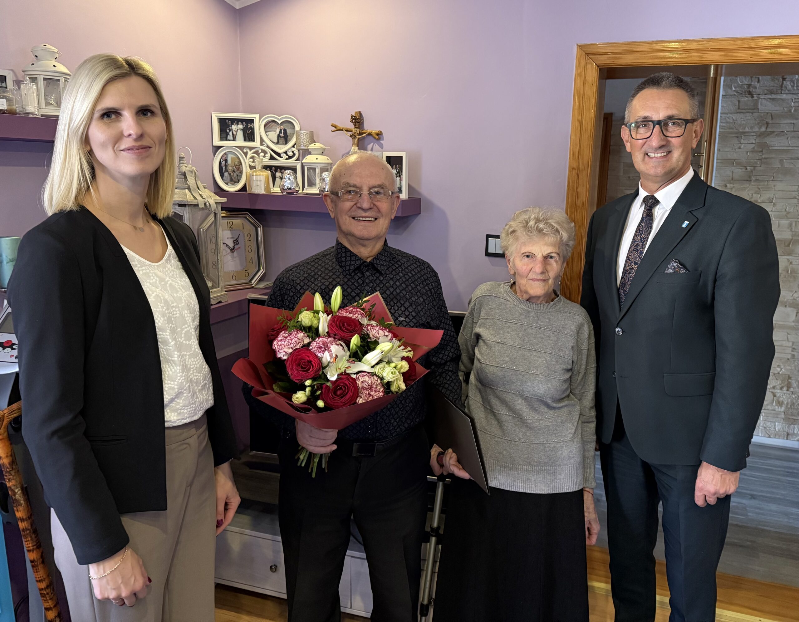 Grupowe zdjęcie, na którym znajdują się wójt, zastępca kierownika USC oraz jubilat wraz z małżonką. Jubilat pozuje z bukietem kwiatów.