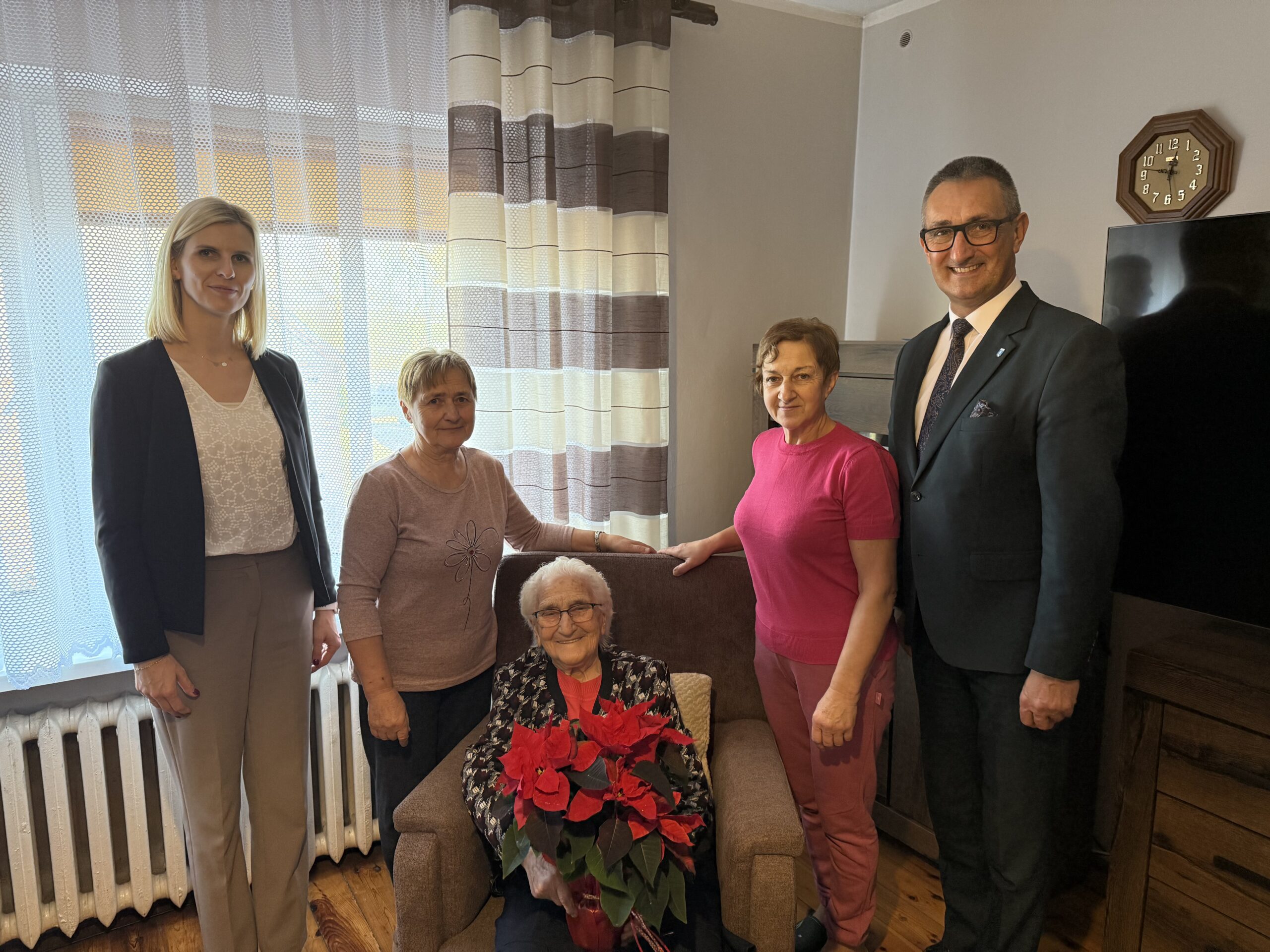 Na fotografii wójt, zastępca kierownika USC oraz seniorka wraz ze swoimi córkami. Pani Zofia pozuje z kwiatem - gwiazdą betlejemską.