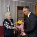 Na fotografii widoczny wójt, który składa jubilatce życzenia i wręcza jej bukiet kwiatów.