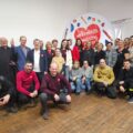Na zdjęciu uwieczniono organizatorów i osoby zaangażowane w przygotowanie wydarzenia. Grupa pozuje do wspólnej fotografii na tle logo Wielkiej Orkiestry Świątecznej Pomocy.