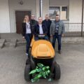 Na fotografii osoby obecne na odbiorze pozują przy nowej kosiarce.