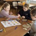 Dwie dziewczynki i chłopiec wykonują prace plastyczne.