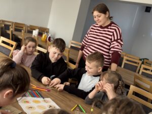 Dwóch chłopców gra w kółko i krzyżyk. Kobieta i dzieci obserwują grę.