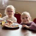 Dwie dziewczynki jedzą pizzę i pozują do zdjęcia.