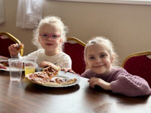 Dwie dziewczynki jedzą pizzę i pozują do zdjęcia.