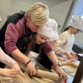 Kobieta pomaga dziewczynce wałkować ciasto na pizzę.