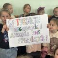 Na zdjęciu widoczne dzieci, które pozują z transparentem, na którym widnieje napis: "W turnieju wygrywajcie i marzenia swe spełniajcie!"