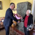 Na zdjęciu widoczny wójt, który wręcza jubilatce bukiet kwiatów.